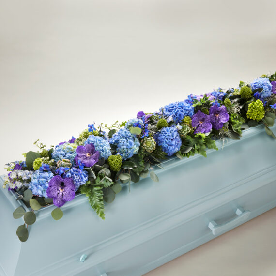 En blomsterdekorasjon på lokket av en kiste med diverse planter i forskjellige farger.