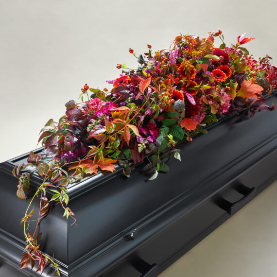 En blomsterdekorasjon av diverse planter i forskjellige farger på toppen av en sort kiste.